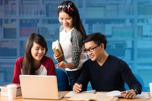 Three students collaborating around a laptop and notebooks during a group study session