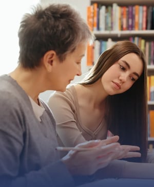 A female college counselor with short gray hair having an earnest discussion with a young female student in front of a bookshelf.