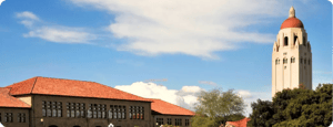 A panoramic view of the Stanford University campus featuring Hoover Tower with its red dome and sandstone buildings under a blue sky.